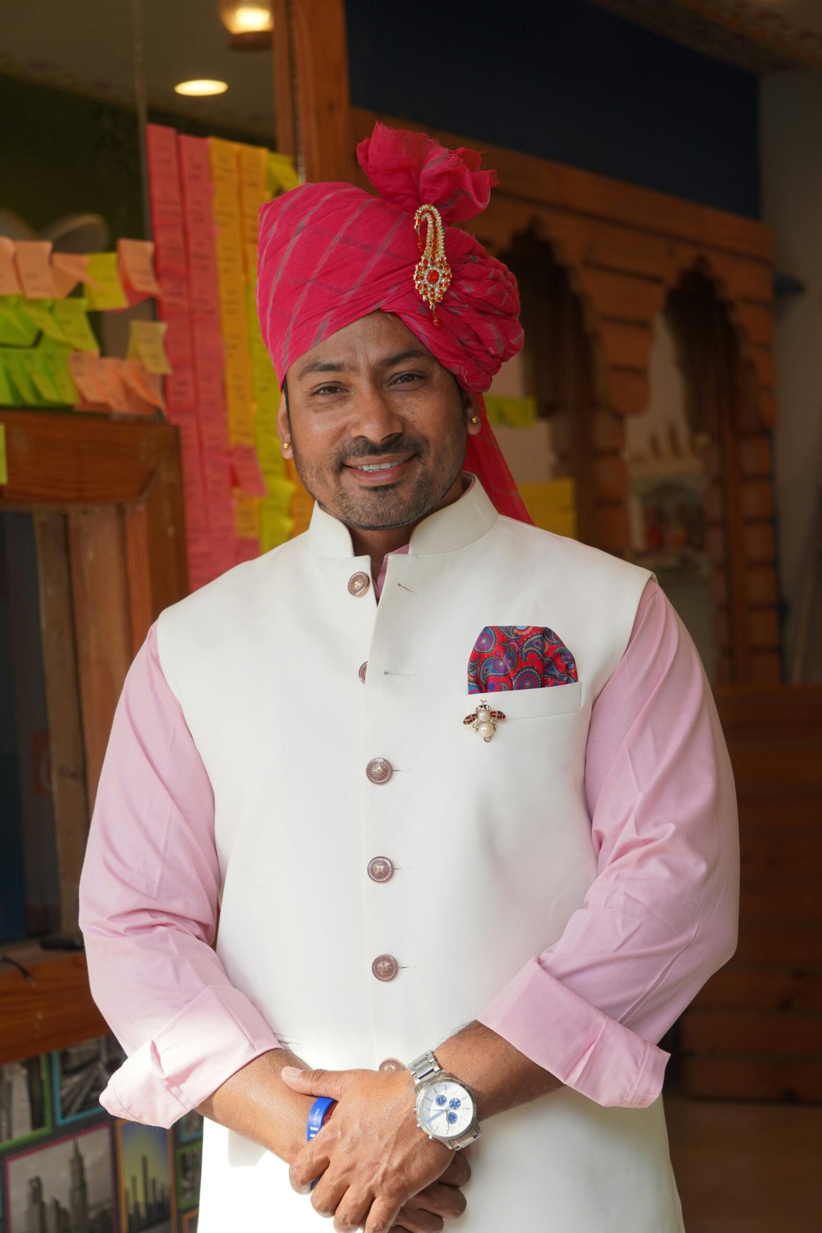 Smiling man in traditional Indian attire with pink turban standing indoors